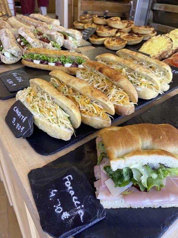 La gamme du midi en vitrine : sandwichs crudités sur baguette et sur focaccia, quiches individuelles, posés sur des ardoises.