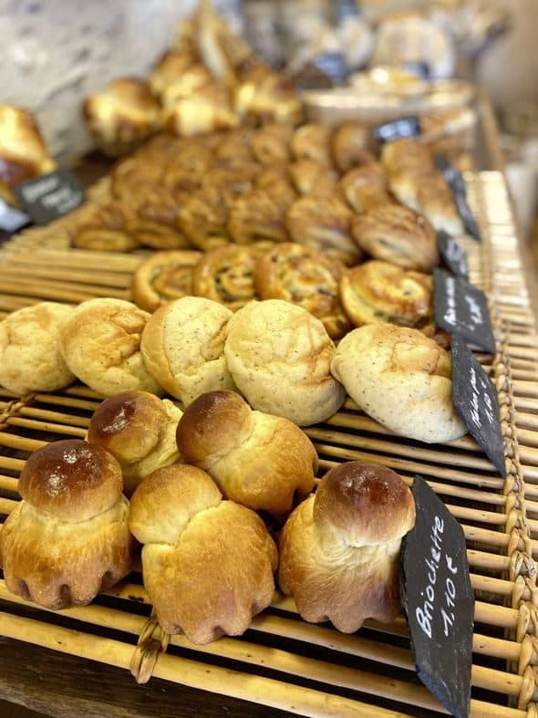 Corbeilles de viennoiseries : brioches à tête dorées au premier plan, melonpan et palmiers derrière.